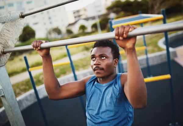 Retrato de determinado desportivo jovem afro-americano realiza exercícios pull-ups para fortalecer os músculos no parque de ginásio ao ar livre — Fotografia de Stock