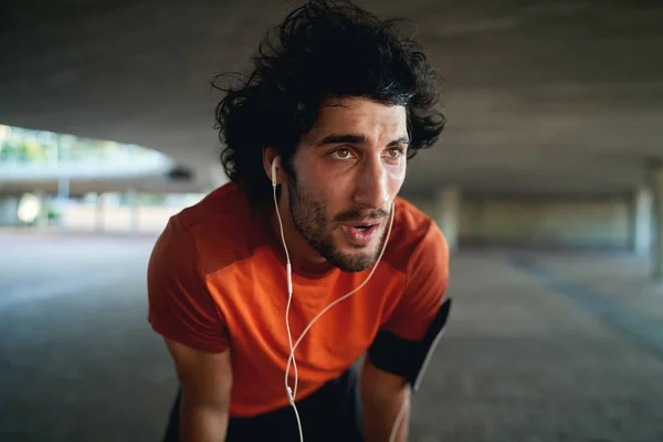 Close-up de um homem cansado corredor com fone de ouvido em seus ouvidos tendo um descanso depois de correr na rua da cidade - resoluções de novos anos — Fotografia de Stock