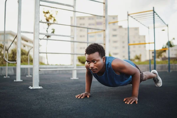 Formda genç Afro-Amerikan bir adam. Çapraz formda antrenman yapıyor. Jimnastik parkında şınav çekiyor.