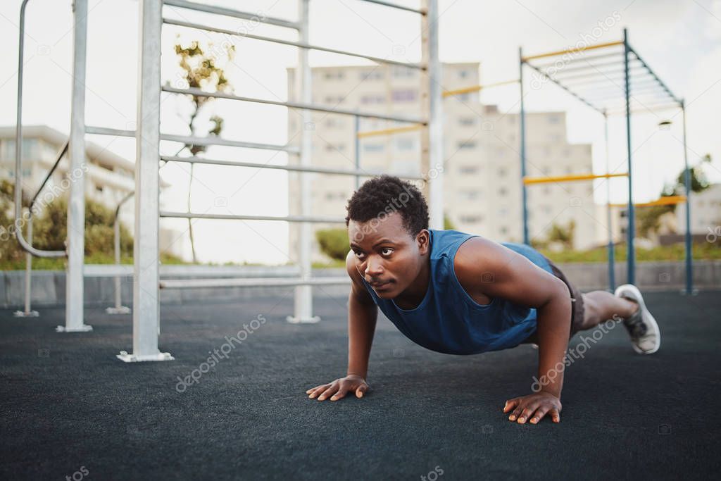 Fit young african american man working out on crossfit strength training doing push ups at the calisthenics park