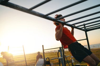 Açık hava spor salonunda barfiks çeken zinde genç bir adam.