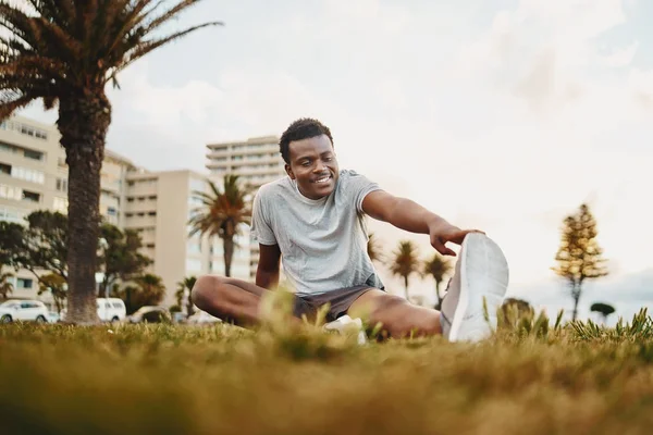 Retrato sonriente de un atleta joven sentado sobre hierba verde haciendo ejercicio de estiramiento en el parque —  Fotos de Stock