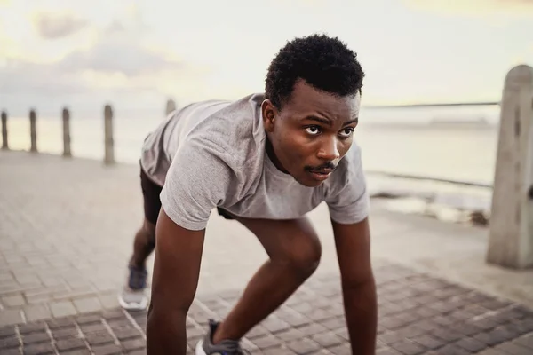 Retrato de um jovem atleta afro-americano em posição inicial preparando-se para correr ao longo do mar — Fotografia de Stock