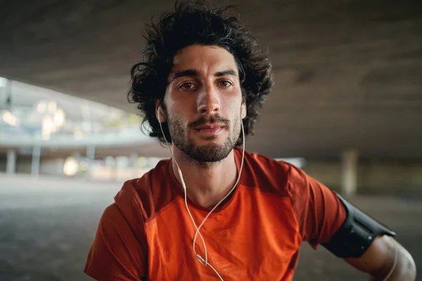 Retrato de un joven atlético deportivo en forma seria con auriculares en sus oídos mirando a la cámara —  Fotos de Stock