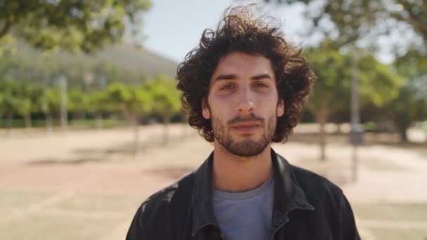 Портрет красивого стильного молодого чоловіка, який дивиться на камеру, стоячи в парку — стокове відео