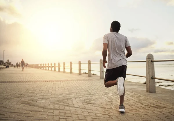 Vista trasera de un joven atleta corriendo en el paseo marítimo por la mañana —  Fotos de Stock