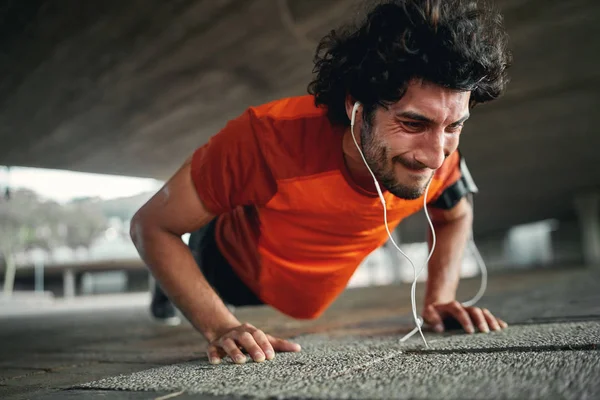 Giovane sportivo con auricolari con espressione del viso dolorosa spremuto ultimo push up - atleta altamente motivato e determinato — Foto Stock