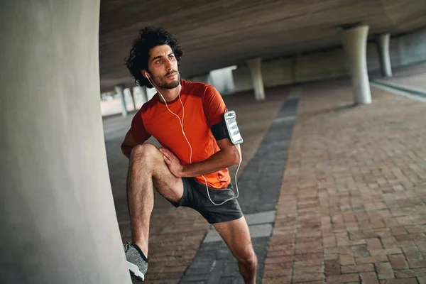 Porträt eines schwergewichtigen jungen Mannes, der sein Bein unter der Brücke ausstreckt, bevor er morgens joggt — Stockfoto