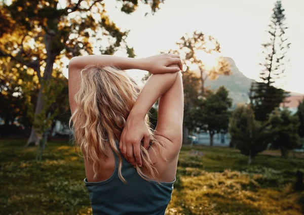 Vista trasera de la joven rubia en ropa deportiva estirando su brazo en el parque - mujer deportiva estirándose en el parque — Foto de Stock