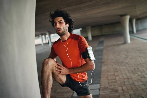 Porträt eines kaukasisch fitten Mannes mit Kopfhörern in den Ohren, der sich vor dem Sport im Freien aufwärmt, indem er das Bein streckt — Stockfoto