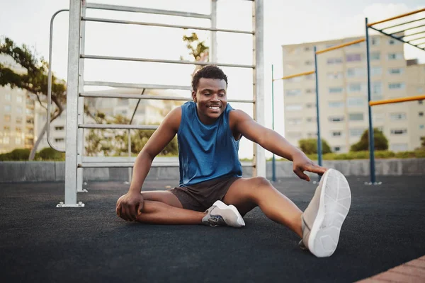 Retrato de un corredor sonriente sentado en el parque de gimnasia al aire libre estirando las piernas preparándose para el entrenamiento de carrera —  Fotos de Stock