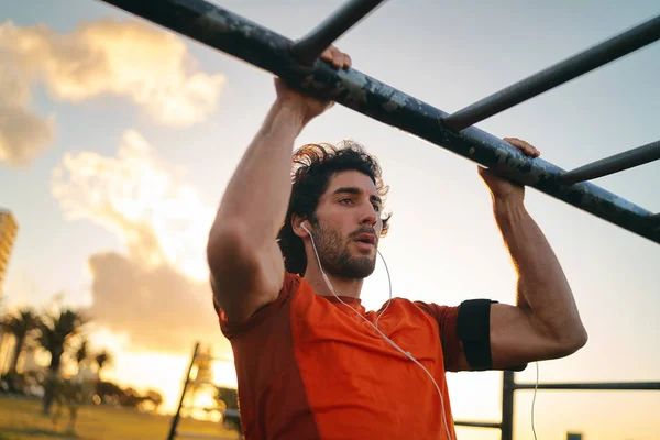 Fitness saludable joven escuchando música en los auriculares haciendo pull-ups en el parque de gimnasio al aire libre - hombre haciendo barbilla-ups —  Fotos de Stock