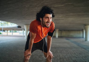 Portrait of sweaty and tired young male fit person taking a break after jogging in city street under the bridge