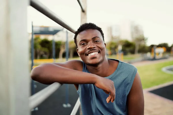 Retrato sonriente de un joven afroamericano deportivo apoyado en un bar en el parque público mirando a la cámara con una gran sonrisa —  Fotos de Stock