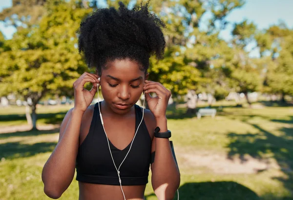 Close-up van een atletische jonge Afro-Amerikaanse vrouw die oortjes in haar oren stopt en naar muziek luistert in het park voordat ze wat fitness doet — Stockfoto