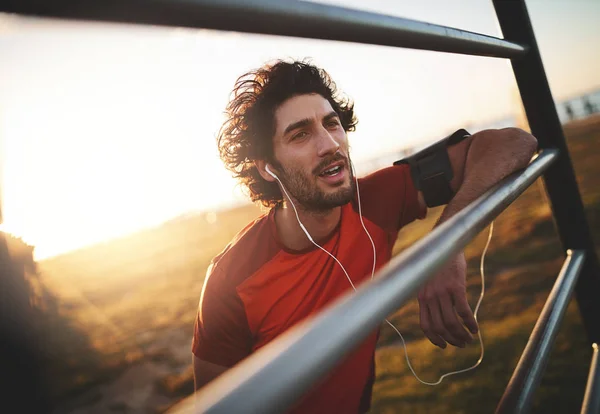 Retrato de un joven atleta disfrutando escuchando música en sus auriculares tomando un descanso después de correr en un día soleado — Foto de Stock