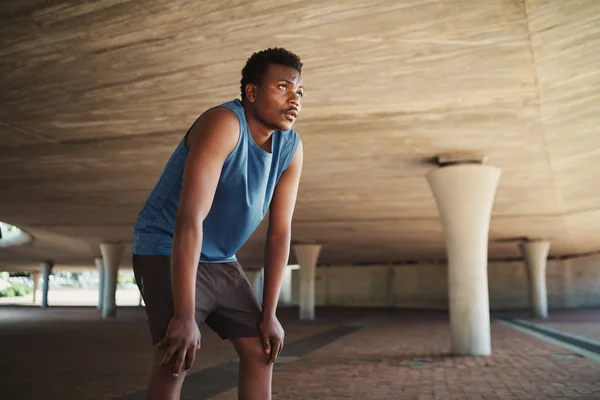 Agotado corredor masculino tomando un descanso después de correr duro en la calle bajo un puente de hormigón —  Fotos de Stock