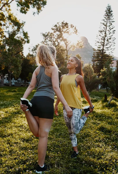 Atleta sorridente che fa esercizio di stretching con le sue amiche nel parco - due amiche che si allenano nel parco — Foto Stock