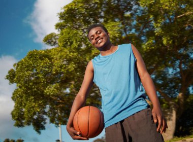 Low angle view of a confident male basketball player holding ball in hand looking to camera