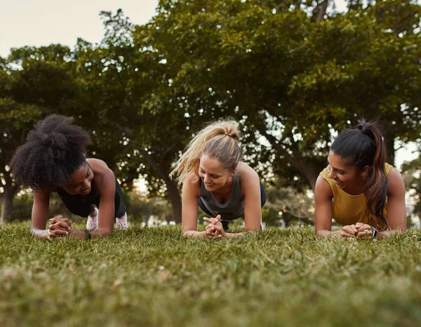 Three multiethnic smiling young active and sporty women doing plank exercises in the park - three woman being active outdoors — Stockfoto