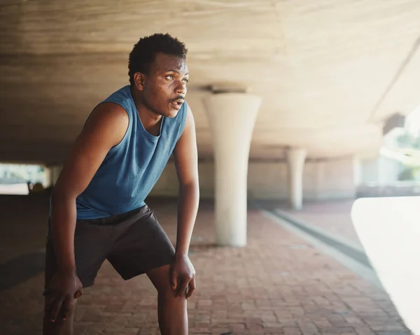 Un afroamericano corredor masculino agarrando respirar después de correr por la calle bajo el puente en la mañana —  Fotos de Stock