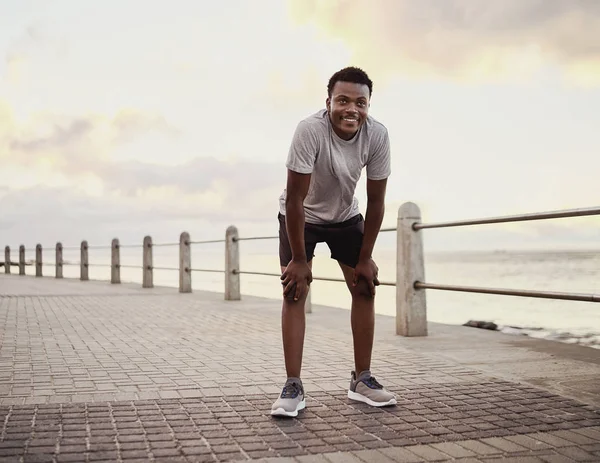 Retrato de un joven deportivo sonriente cansado tomando un descanso después de trotar en el paseo marítimo —  Fotos de Stock