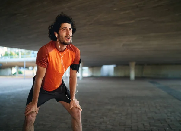 Retrato de un atleta caucásico cansado escuchando música respirando después de una larga carrera bajo el puente —  Fotos de Stock