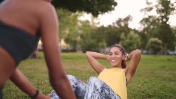 Sorridente amico afro-americano che sostiene Fit giovane donna sdraiata su erba verde per fare esercizio di fitness crunch al parco — Video Stock