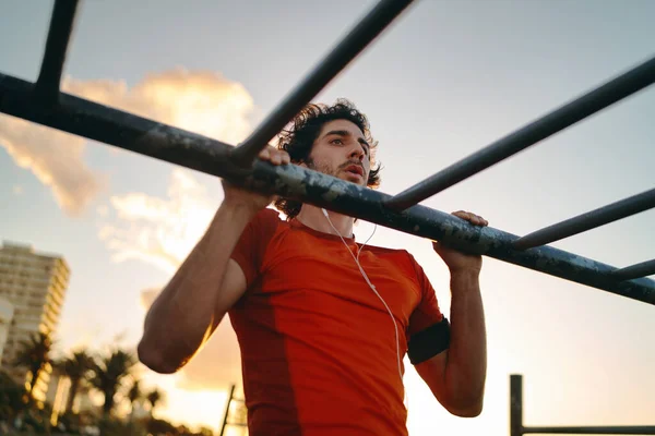 Close-up de um jovem atleta do sexo masculino fazendo exercícios no bar no parque de ginástica contra o céu homem fazendo pull-ups ao ar livre — Fotografia de Stock