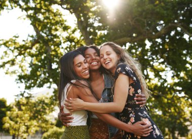 Portrait of happy three multiethnic multiracial female friends closely hugging and showing care and love for each other in park clipart