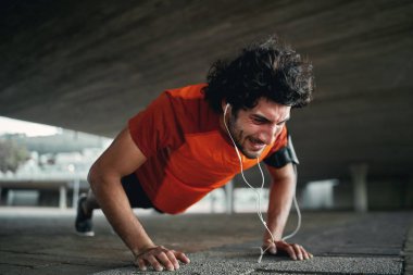 Güçlü ve yüksek motivasyona sahip genç sporcu kaldırımda şınav çekiyor.