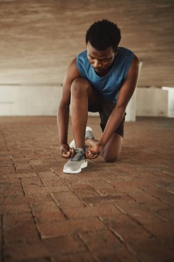 Fitness young man in sportswear tying shoelaces of sporty sneaker on pavement