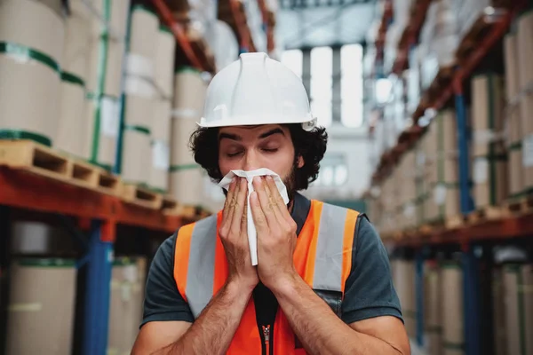 Ung lagerchef hostar och nyser medan du mår illa och täcker munnen med näsduk stående i fabriken — Stockfoto