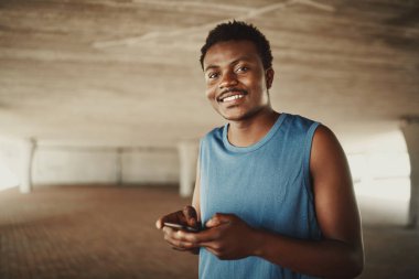 Male runner holding mobile phone in hand smiling and looking to camera at outdoors