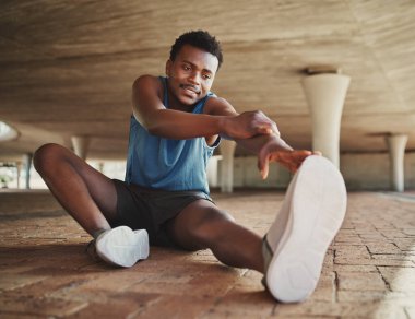 Genç erkek koşucu, köprünün altında koşmadan önce ısınıyor ve esniyor.