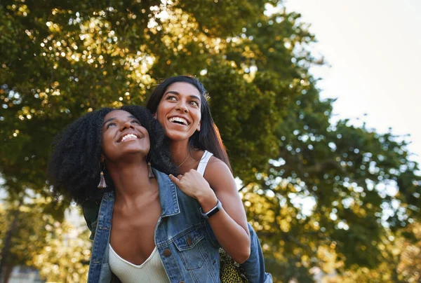 Retrato de una joven afroamericana sonriente dando un paseo a cuestas a su mejor amiga en el parque en un día soleado - grupo de estudiantes universitarios riendo y divirtiéndose en el campus — Foto de Stock