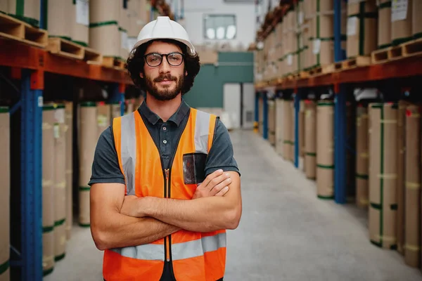 Ritratto di lavoratore fiducioso che indossa casco e occhiali con uniforme giubbotto arancione in piedi in corridoio del magazzino di fabbrica resistente — Foto Stock