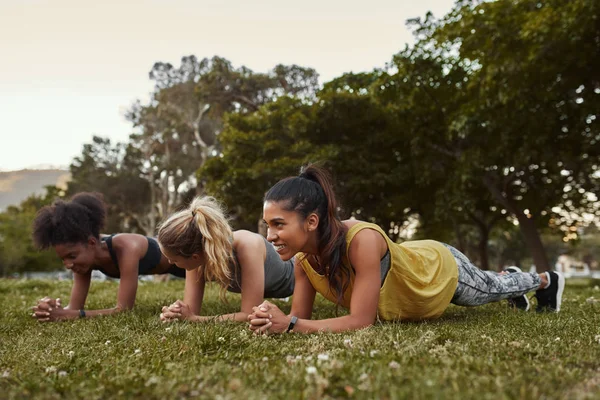 Giovane sorridente in forma tre diverse donne multirazziali in abbigliamento sportivo facendo esercizi di tavola su erba verde nel parco in una giornata di sole — Foto Stock