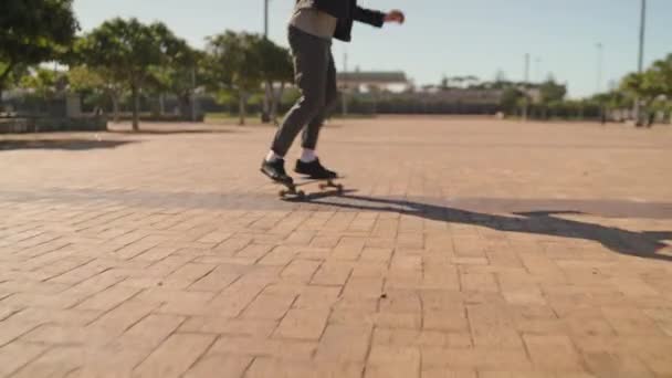 Κοντινό πλάνο ενός αρσενικού skateboarders πόδια ιππασία σε ένα skateboard πάνω από το πεζοδρόμιο στο πάρκο — Αρχείο Βίντεο