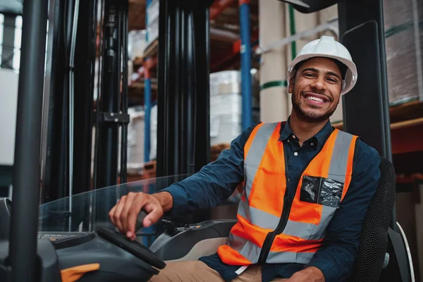 Giovane autista di carrelli elevatori seduto nel veicolo in magazzino sorridente guardando la fotocamera — Foto Stock