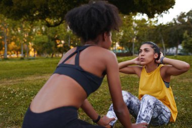Fit young woman doing crunches with her exercise female partner on green grass during a workout session - young determined and motivated woman doing exercise