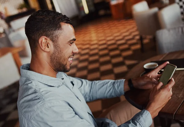 Молодий веселий африканський чоловік з чашкою кави і читанням текстового повідомлення на своєму мобільному телефоні — стокове фото