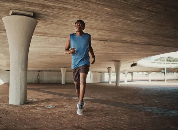 Hombre atlético corriendo durante la mañana bajo el puente de hormigón en el pavimento —  Fotos de Stock