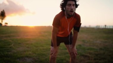 Male runner standing bent over and catching his breath after a running session in the park