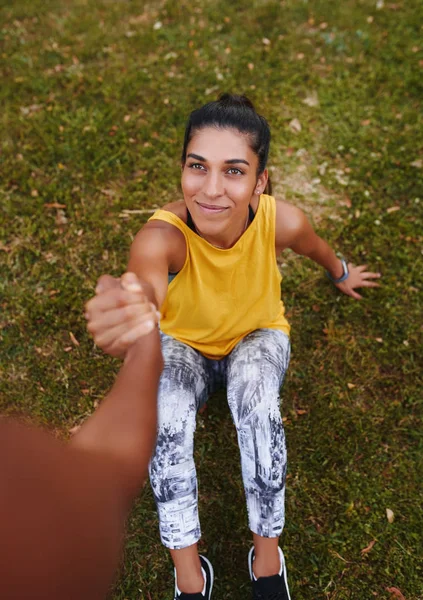 Vista alta de una joven fitness sonriente sentada sobre hierba verde sosteniendo firmemente la mano de sus amigas - amiga que ofrece una mano de ayuda — Foto de Stock