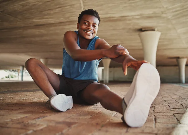 Pemandangan di depan seorang pemuda yang tersenyum dan fit mengenakan sepatu olahraga yang meregangkan kakinya sebelum berlari di kota — Stok Foto