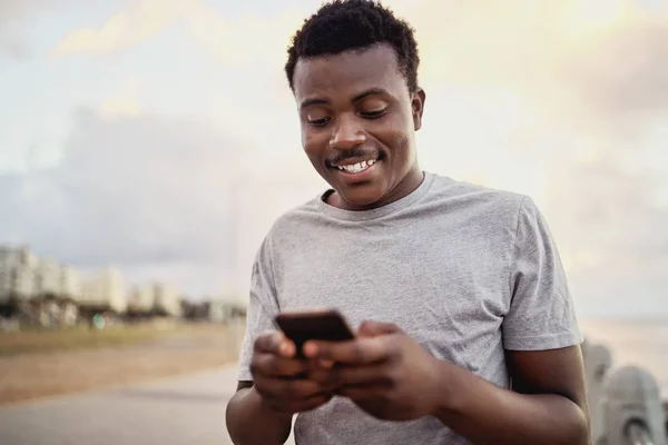 Retrato de um jovem atleta feliz mensagens de texto no telefone inteligente em pé contra o fundo da cidade — Fotografia de Stock