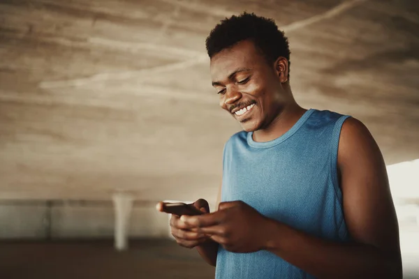 Un hombre joven afroamericano en forma mensajes de texto en el teléfono móvil al aire libre — Foto de Stock