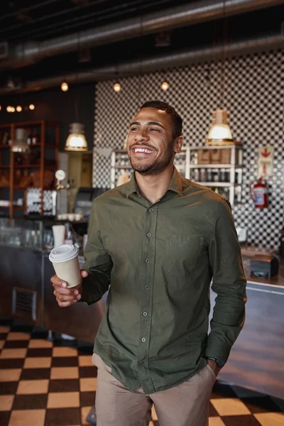 Bonito jovem afro-americano segurando takeaway caneca de café em pé no café — Fotografia de Stock
