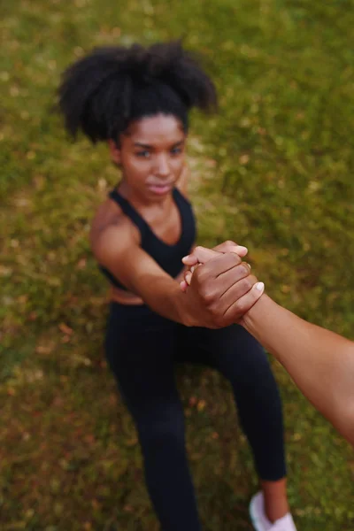 Amigos dando uma mão amiga a uma jovem mulher afro-americana fitness para se levantar do chão após o exercício — Fotografia de Stock